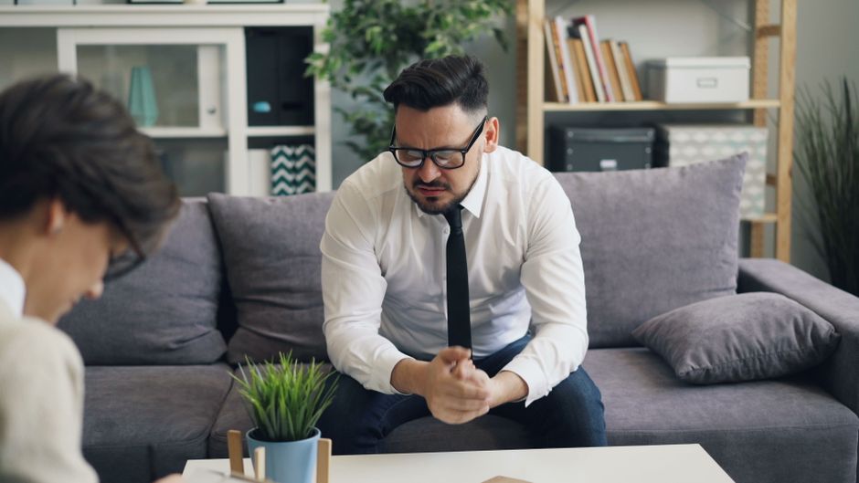 A stressed businessman in therapy session, showing visible emotions on a sofa. - Photo by Vitaly Gariev on Pexels