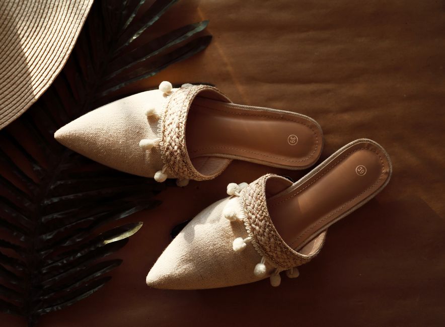 Stylish beige sandals with decorative pom-poms on a summer backdrop, featuring woven straw elements. - Photo by Nada Bastawi on Pexels