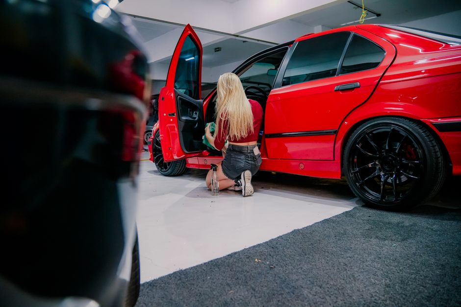 A woman kneels, cleaning the interior of a red BMW in a garage environment. - Photo by Caio Renato de Campos on Pexels